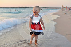 Happy little girl standing barefoot on the wet sand on the beach