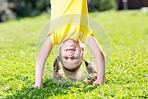 Happy little girl standing on her head on green lawn.