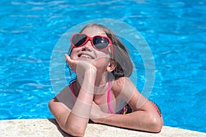 Happy little girl in sunglasses in pool on sunny day. Childhood, dreams and summer concept