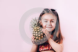 Happy little girl in swim suit holding pineapple.