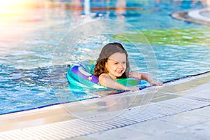 Happy little girl swimming in the pool with inflatable ring on a Sunny summer day. Kids learn to swim. Family vacation