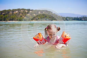 Happy little girl swimming with water wings in the lake called Etang de la Bonde in France photo