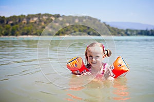 Happy little girl swimming with water wings in the lake called Etang de la Bonde in France photo
