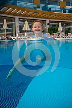 Happy little girl swims in the pool in summer with inflatable ring. Child learning to swim in outdoor pool of luxury