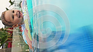 Happy little girl swims in the pool in summer with inflatable ring. Child learning to swim in outdoor pool of luxury