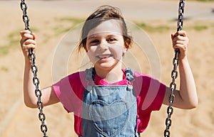 Happy little girl swinging on swing at playground