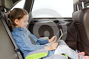 Happy little girl with tablet pc driving in car