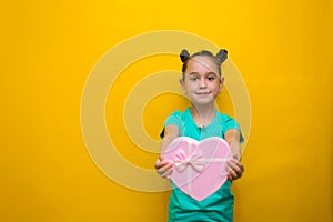 Happy little girl with tails standing isolated over yellow background holding shopping pink bag. smiles thoughtfully