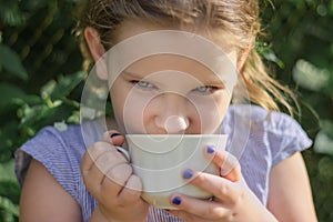 Happy little girl tastes aromatic flower tea from white cup