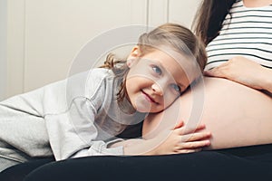 Happy little girl touching her pregnant mom tummy. Pregnant mother and daughter spending time together at home