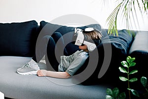 Happy little girl with virtual reality headset lying on sofa at home