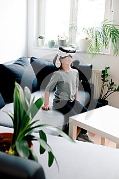Happy little girl with virtual reality headset sitting on sofa and watching high