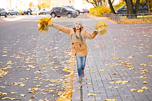 Happy little girl walking on the curb through the fallen leaves on a sidewalk in autumn city