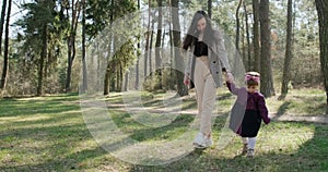 Happy little girl walking and playing with mother among trees in coniferous forest. Healthy child family recreation in