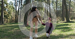 Happy little girl walking and playing with mother among trees in coniferous forest. Healthy child family recreation in