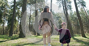 Happy little girl walking and playing with mother among trees in coniferous forest. Healthy child family recreation in