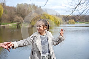 Happy little girl walks in nature, holding dad`s hand