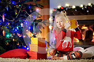 Happy little girl wearing Christmas pajamas playing by a fireplace in a cozy dark living room on Christmas eve