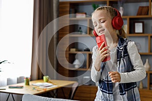 Happy little girl wearing red earphones dancing and singing using smartphone like microphone. Cute child having fun