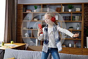 Happy little girl wearing red earphones dancing and singing using smartphone like microphone. Cute child having fun