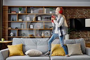 Happy little girl wearing red earphones dancing and singing using smartphone like microphone. Cute child having fun