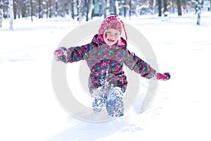 Happy little girl wearing a warm clothes running through the snowdrifts in snowy park on cheerful wint