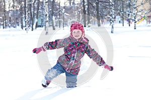 Happy little girl wearing a warm clothes walking through the snowdrifts in snowy park on cheerful wint