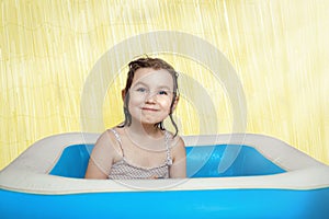 Happy little girl with wet hair sits in a children`s swimming pool