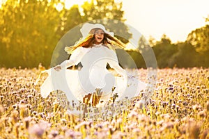 Happy little girl in a white dress running on field at sunset