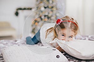 Happy little girl in a white sweater and blue jeans posing near christmas tree