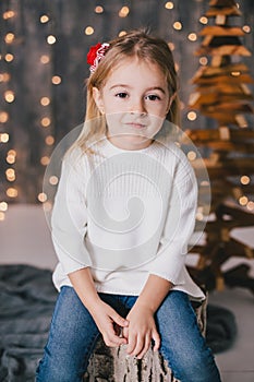 Happy little girl in a white sweater and blue jeans posing near christmas tree