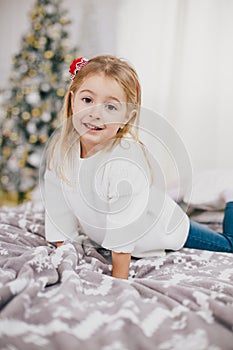 Happy little girl in a white sweater and blue jeans posing near christmas tree