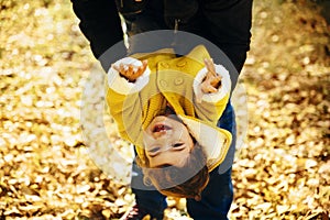 Happy little girl in yellow jacket playing with her father in park. Child smiling and hanging in autumn forest. Family time fun in