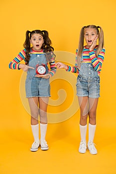 Happy little girls hold vintage alarm clock on yellow background. Small children smiling with mechanical clock. School