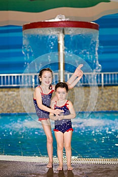 Happy little girls in identical swimsuits posing near the children`s pool in the water Park. Child learns to swim