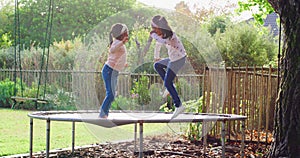 Happy little girls jumping on a trampoline on a sunny day. Two energetic and excited young siblings playing and having