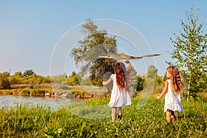 Happy little girls with kite running on meadow in spring park. Children having fun playing outdoors