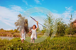 Happy little girls with kite running on meadow in summer park. Children having fun playing outdoors