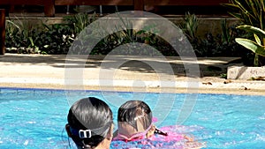 Happy little girls learn to swim in the pool with her mother on a hot summer day during vacation.