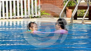 Happy little girls learn to swim in the pool with her mother on a hot summer day during vacation.