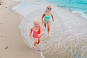 Happy little girls play with water on beach, kids have fun