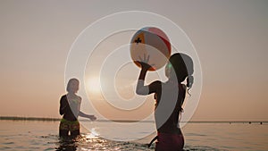 Happy little girls playing air ball in water at sunset, having fun outdoors