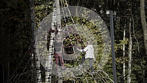 Happy little girls playing on the playground. Action. Kids having fun with the climbing net outdoors near green early