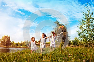 Happy little girls running with kite in summer park while thir mother helps them. Children having fun playing outdoors