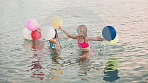 Happy little girls running together with balloons through the water