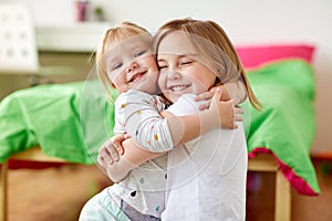 Happy little girls or sisters hugging at home