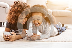 Happy little girls with smartphones lying on floor