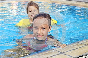 Happy little girls swimming and smiling in outdoor pool at sunset