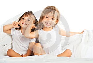 Happy little girls twins sister in bed under the blanket having