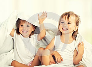 Happy little girls twins sister in bed under the blanket having